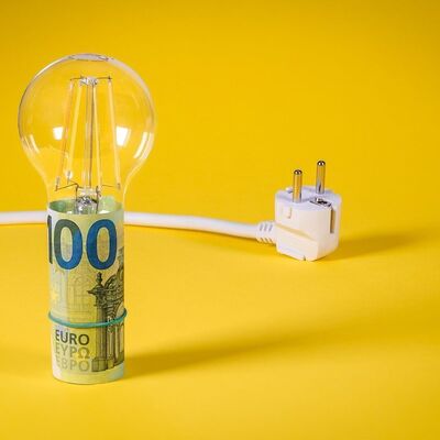 Das Bild zeigt eine Glühlampe und einen Stecker. Die Glühlampe ist an der Fassung mit einem Geldschein umwickelt. 