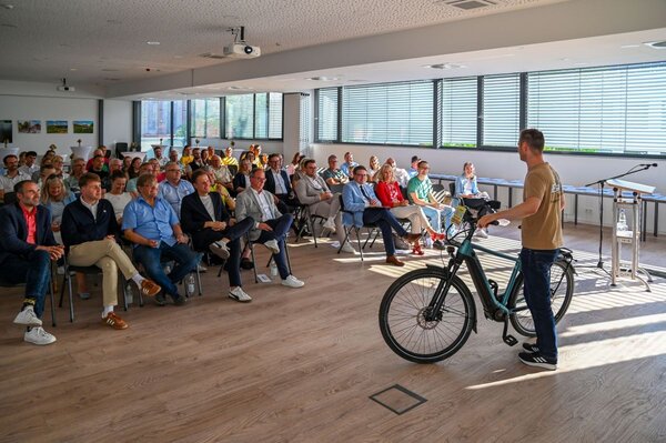 Das Bild zeigt Marvin Esser, Gesch&auml;ftsf&uuml;hrer der Firma 2-Rad Esser GmbH & Co. KG, gemeinsam mit den Teilnehmenden bei der Pr&auml;mierungsveranstaltung der Aktion Stadtradeln im gro&szlig;en Sitzungssaal des Landratsamtes Main-Tauber-Kreis. Er erkl&auml;rt in seinem Vortrag unter anderem die richtigen ergonomischen Einstellungen am Fahrrad. 
